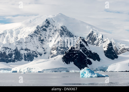 Iceberg bleu détroit de Gerlache Antarctique // DÉTROIT DE GERLACHE, Antarctique — de grandes montagnes s'élèvent de la rive du détroit de Gerlache, sur le côté ouest de la péninsule Antarctique, alors qu'un petit iceberg bleu flotte au premier plan. Cette région est réputée pour ses paysages époustouflants et est fréquemment traversée par des expéditions antarctiques. Banque D'Images