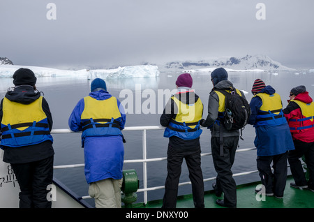 Antarctique passagers Cuverville Island Landscape View // les passagers prêts dans leurs gilets de sauvetage admirent la vue sur le paysage en attendant de monter à bord des bateaux pneumatiques Zodiac pour se rendre à terre sur l'île de Cuverville sur le côté ouest de la péninsule Antarctique. Banque D'Images