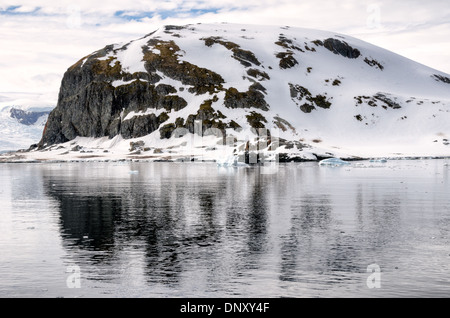 L'ANTARCTIQUE - Montagnes rocheuses escarpées réfléchir sur les eaux encore près de Cuverville Island sur la péninsule antarctique. Le sommet de la montagne est couverte d'un vert foncé et marron mousse, ce qui est inhabituel pour la région. Banque D'Images