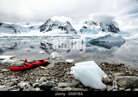 L'ANTARCTIQUE - un kayak tandem rouge vif est tiré vers le haut sur la côte rocheuse de l'île de Cuverville, l'Antarctique, avec eaux miroitant dans le fond couvert d'icebergs et brash. Banque D'Images