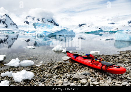 Un kayak tandem rouge vif est tiré vers le haut sur la côte rocheuse de l'île de Cuverville, l'Antarctique, avec eaux miroitant dans le fond couvert d'icebergs et brash. Banque D'Images