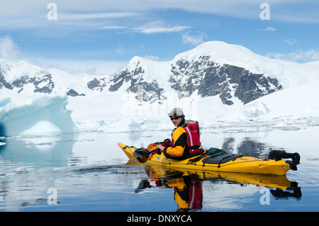Kayakiste maritime Île Cuverville Péninsule Antarctique Été | ÎLE CUVERVILLE, Antarctique — Un kayakiste maritime se repose sur des eaux calmes comme un miroir au milieu des icebergs au large de l'île Cuverville sur la péninsule antarctique, les sommets enneigés du détroit de Gerlache s'élevant en arrière-plan. Cuverville abrite l'une des plus grandes colonies de manchots pygosceles (Pygoscelis papua) de la péninsule, et le kayak est le seul moyen pour les touristes d'approcher légalement le rivage au niveau de l'eau conformément aux directives des visiteurs du Traité antarctique. Banque D'Images