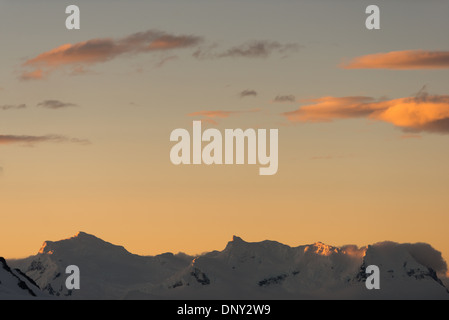 L'ANTARCTIQUE - le soleil couchant jette une lueur orange magnifique sur les nuages et les montagnes de l'Antarctique spectaculaire paysage de Paradise Harbour, l'Antarctique. Banque D'Images