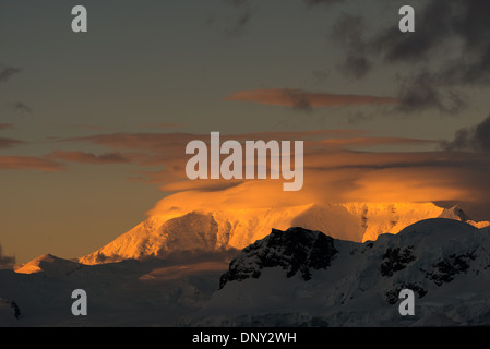 L'ANTARCTIQUE - le soleil couchant jette une lueur orange magnifique sur les nuages et les montagnes de l'Antarctique spectaculaire paysage de Paradise Harbour, l'Antarctique. Banque D'Images