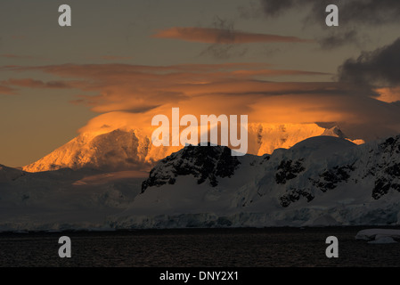 L'ANTARCTIQUE - le soleil couchant jette une lueur orange magnifique sur les nuages et les montagnes de l'Antarctique spectaculaire paysage de Paradise Harbour, l'Antarctique. Banque D'Images