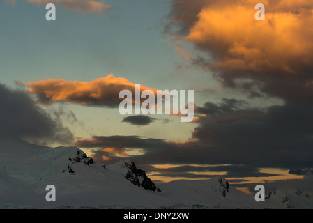 L'ANTARCTIQUE - le soleil couchant jette une lueur orange magnifique sur les nuages et les montagnes de l'Antarctique spectaculaire paysage de Paradise Harbour, l'Antarctique. Banque D'Images