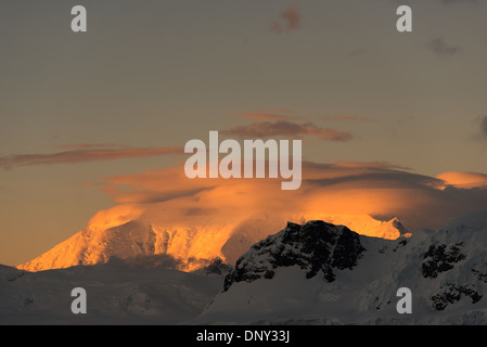 L'ANTARCTIQUE - le soleil couchant jette une lueur orange magnifique sur les nuages et les montagnes de l'Antarctique spectaculaire paysage de Paradise Harbour, l'Antarctique. Banque D'Images