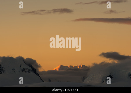 L'ANTARCTIQUE - le soleil couchant jette une lueur orange magnifique sur les nuages et les montagnes de l'Antarctique spectaculaire paysage de Paradise Harbour, l'Antarctique. Banque D'Images