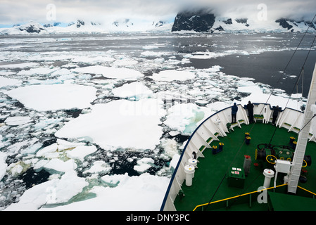 CHENAL LEMAIRE, Antarctique — un navire d'expédition renforcé par la glace navigue dans la glace de mer à l'entrée nord du chenal Lemaire. Le passage étroit, surnommé « Kodak Gap » pour ses paysages spectaculaires, est un itinéraire clé le long de la péninsule Antarctique pour les navires de tourisme et de recherche. Les conditions de glace dans ce chenal peuvent varier considérablement et parfois empêcher complètement le passage. Banque D'Images