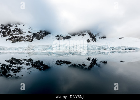 LEMAIRE CHANNEL, Antarctique — des reflets miroirs parfaits de montagnes et de falaises à Glandaz point sur Booth Island créent une scène symétrique dans les eaux exceptionnellement calmes. Ces conditions vitreuses dans le canal Lemaire, surnommé « Kodak Gap », sont rares dans cette région typiquement balayée par le vent de la péninsule Antarctique. Les eaux calmes créent un miroir naturel du paysage antarctique spectaculaire. Banque D'Images