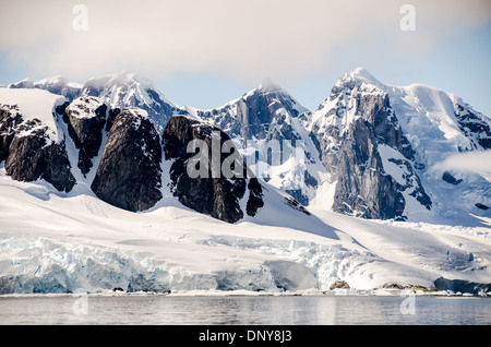 Petermann Island montagnes enneigées Antarctique // PETERMANN ISLAND, Antarctique — Une vue panoramique des montagnes rocheuses abruptes et enneigées vues depuis l'île Petermann en Antarctique. L'île est connue pour ses falaises rocheuses spectaculaires bordées de glace et de neige, offrant un contraste saisissant avec le paysage glacé environnant. D'imposantes falaises dominent la scène, soulignant la beauté sauvage de cet endroit reculé de l'Antarctique. Petermann Island est un endroit populaire pour observer la faune, y compris les pingouins et les phoques, que l'on trouve couramment le long de ses rives. Banque D'Images