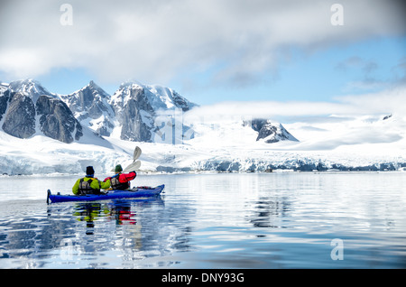 ÎLE PETERMANN, Antarctique — les kayakistes pagayent dans des eaux vitreuses et miroirs le long du littoral montagneux pittoresque près de l'île Petermann, sur le côté ouest de la péninsule Antarctique. Les conditions calmes offrent des reflets parfaits des sommets enneigés, créant une symétrie étonnante entre ciel et mer dans ce paysage polaire immaculé. Banque D'Images