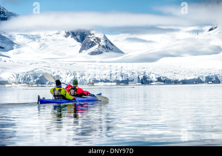 ÎLE PETERMANN, Antarctique — les kayakistes pagayent dans des eaux vitreuses et miroirs le long du littoral montagneux pittoresque près de l'île Petermann, sur le côté ouest de la péninsule Antarctique. Les conditions calmes offrent des reflets parfaits des sommets enneigés, créant une symétrie étonnante entre ciel et mer dans ce paysage polaire immaculé. Banque D'Images