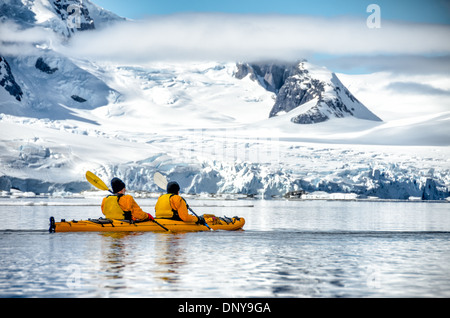 ÎLE PETERMANN, Antarctique — les kayakistes pagayent dans des eaux vitreuses et miroirs le long du littoral montagneux pittoresque près de l'île Petermann, sur le côté ouest de la péninsule Antarctique. Les conditions calmes offrent des reflets parfaits des sommets enneigés, créant une symétrie étonnante entre ciel et mer dans ce paysage polaire immaculé. Banque D'Images