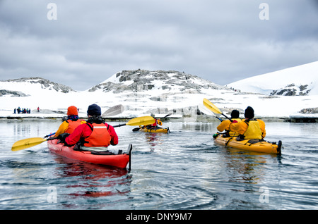 ÎLE PETERMANN, Antarctique — les kayakistes pagayent dans des eaux vitreuses et miroirs le long du littoral montagneux pittoresque près de l'île Petermann, sur le côté ouest de la péninsule Antarctique. Les conditions calmes offrent des reflets parfaits des sommets enneigés, créant une symétrie étonnante entre ciel et mer dans ce paysage polaire immaculé. Banque D'Images