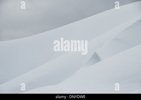 L'ANTARCTIQUE - les couches de neige et de glace forme formes doux sur les pentes d'une montagne à l'île de Melvhior sur le côté ouest de la péninsule antarctique. La neige est fixé contre nuages gris dans le coin supérieur gauche. Banque D'Images