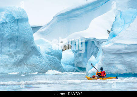 L'ANTARCTIQUE - un kayakiste solo navigue à travers une ouverture entre les grands icebergs bleu dans un cimetière d'iceberg dans une baie à l'île de Melchior sur la péninsule antarctique. Banque D'Images