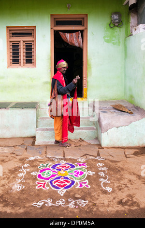 Mendiant mendicité religieuse indienne à l'extérieur d'une maison de village rural en face d'un rangoli. conception festival L'Andhra Pradesh, Inde Banque D'Images