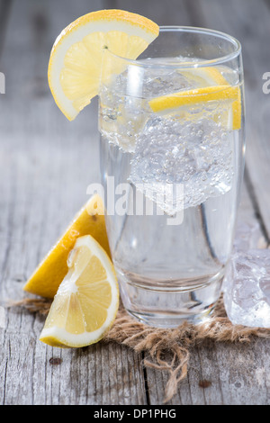 L'eau pétillante avec le citron et la glace sur fond de bois Banque D'Images
