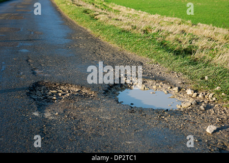 Gros plan de grands nids-de-poule profonds dans la rue de la route remplie d'eau en hiver Angleterre Royaume-Uni GB Grande-Bretagne Banque D'Images