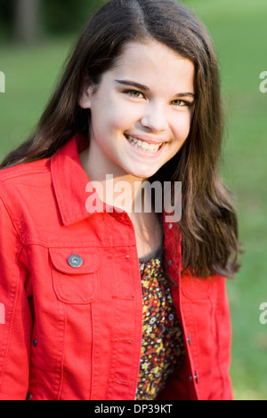 Portrait de pré-ado fille avec de longs cheveux bruns, wearing red jacket, outdoors Banque D'Images