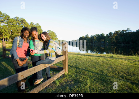 Pre-teen girls sitting on fence, à la tablette à l'ordinateur et téléphone cellulaire, à l'extérieur Banque D'Images