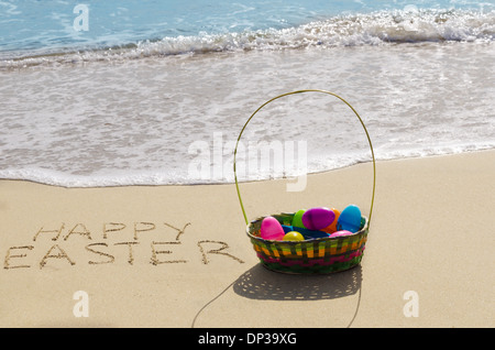 Panneau "Joyeuses Pâques" avec panier et oeufs sur la plage de sable à l'océan Banque D'Images