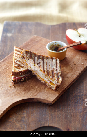 Panini au fromage grillé au fromage et pomme, moitié de pomme rouge et la moutarde de Dijon dans un petit bol sur une planche à découper, Studio Shot Banque D'Images