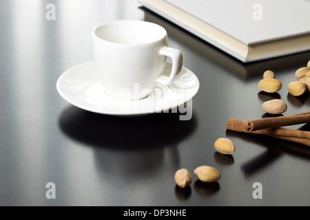 Tasse de café et livre fermé sur la table avec les noix et la cannelle Banque D'Images