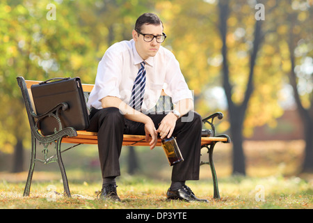 Déçu businessman assis sur un banc en bois avec bouteille à la main, dans le parc Banque D'Images