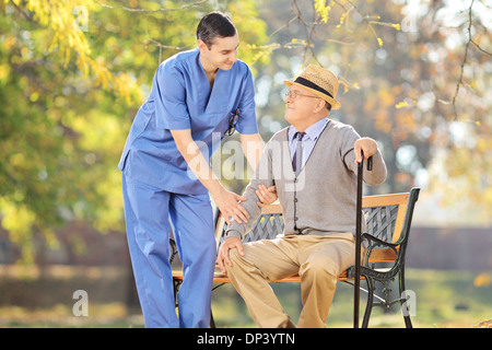 Professionnel de la santé de parler avec de hauts homme assis sur un banc à l'extérieur Banque D'Images