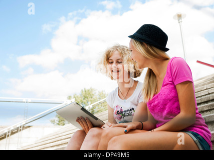 Teenage Girls sitting on stairs outdoors, looking at tablet computer, Allemagne Banque D'Images