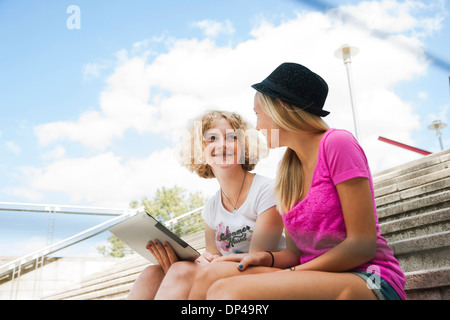 Teenage Girls sitting on stairs outdoors, looking at tablet computer, Allemagne Banque D'Images