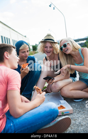 Groupe d'adolescents assis sur le sol à l'extérieur, manger des pizzas et à traîner, Allemagne Banque D'Images