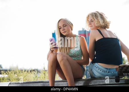 Adolescentes assis sur un banc à l'extérieur, à la recherche de téléphone cellulaire, Allemagne Banque D'Images