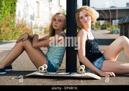 Portrait of teenage girls en plein air avec skateboard, looking at camera, assis dans la rue, Allemagne Banque D'Images