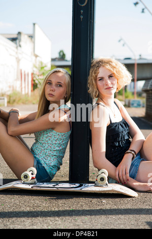 Portrait of teenage girls en plein air avec skateboard, looking at camera, assis dans la rue, Allemagne Banque D'Images