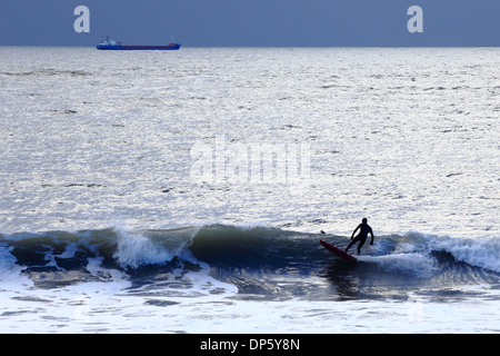 Un sihouetted surfer contre la mer, les balades les vagues sur un mauvais jour d'hiver, ciel couvert à Langland Bay dans le sud marmonne, Wa Banque D'Images