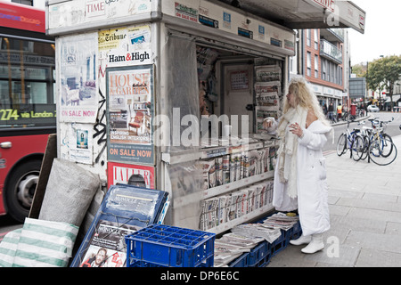 Femme habillée tout en blanc à un kiosque de presse. Banque D'Images