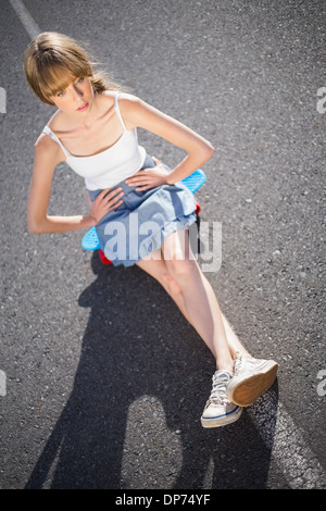 Quartier branché de jeune femme assise sur son skateboard Banque D'Images