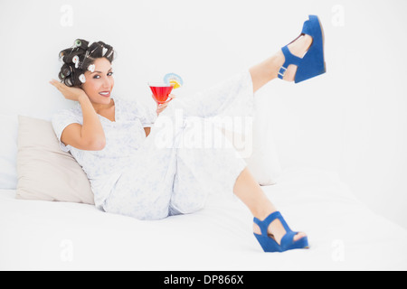 Brunette in hair rollers et wedge shoes holding a cocktail looking at camera Banque D'Images