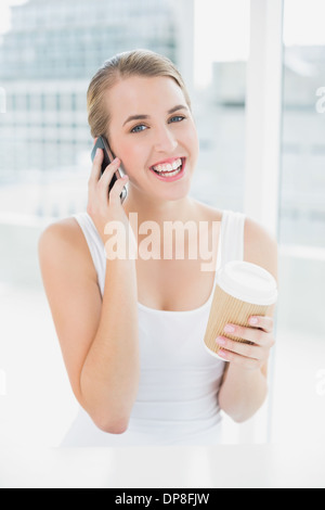 Smiling blonde woman on the phone holding coffee Banque D'Images