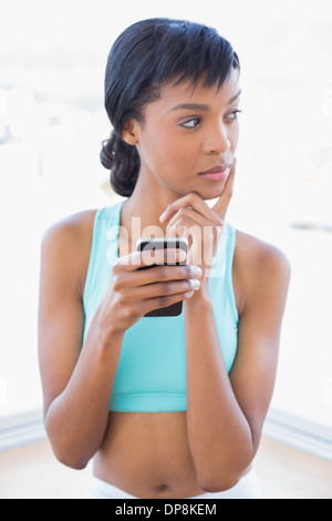 Pensive fit woman holding a mobile phone Banque D'Images