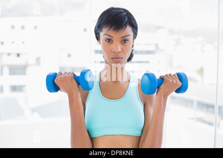 Fronçant black haired woman holding dumbbells Banque D'Images