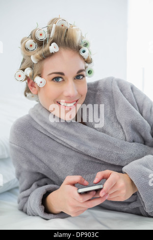 Ambiance joyeuse blonde woman in hair curlers en utilisant son téléphone portable Banque D'Images