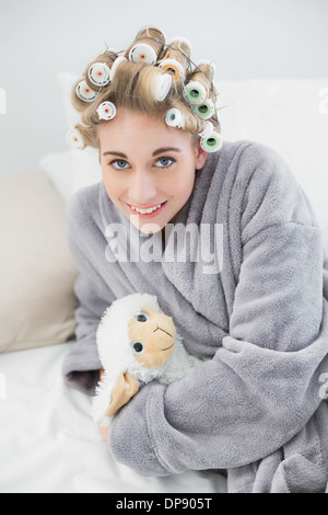 Heureux Détendu blonde woman in hair curlers de câliner un mouton en peluche Banque D'Images