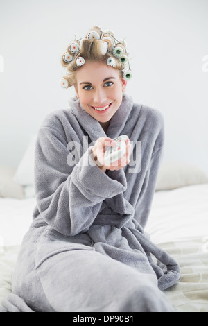 Ambiance joyeuse blonde woman in curlers de cheveux à l'aide d'une télécommande Banque D'Images
