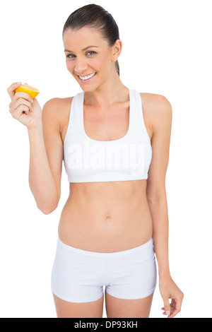 Smiling woman in sportswear holding tranche d'orange looking at camera Banque D'Images