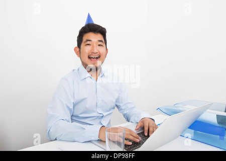 Portrait of happy businessman wearing party hat tandis que working in office Banque D'Images