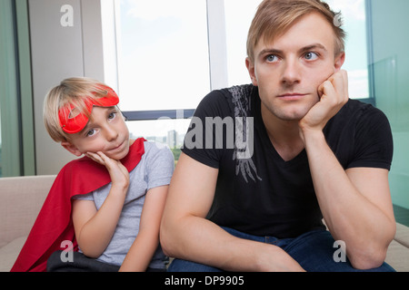 Portrait de triste garçon habillé en costume de super-héro assis avec le père sur le canapé-lit à la maison Banque D'Images